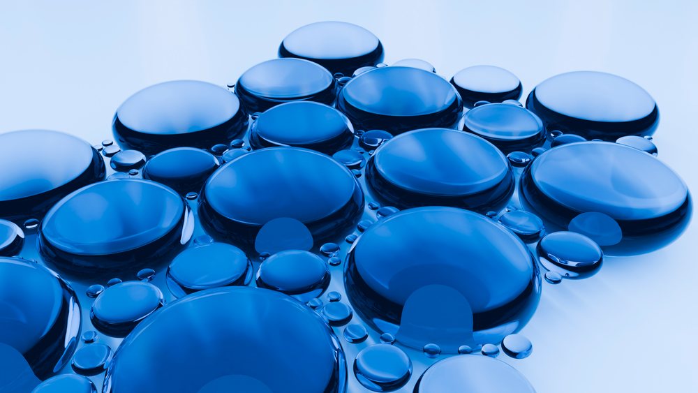 Close-up macro photograph showing numerous blue water droplets clustered with clear reflections on a smooth surface demonstrating surface tension.