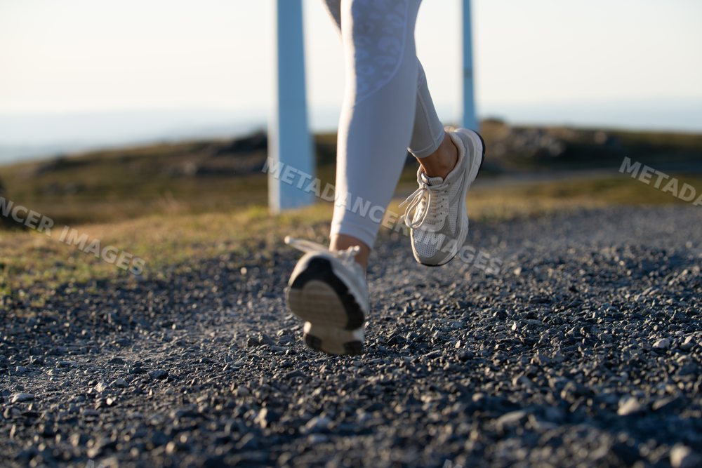 A white woman running on a gravel trail near wind turbines in Galicia