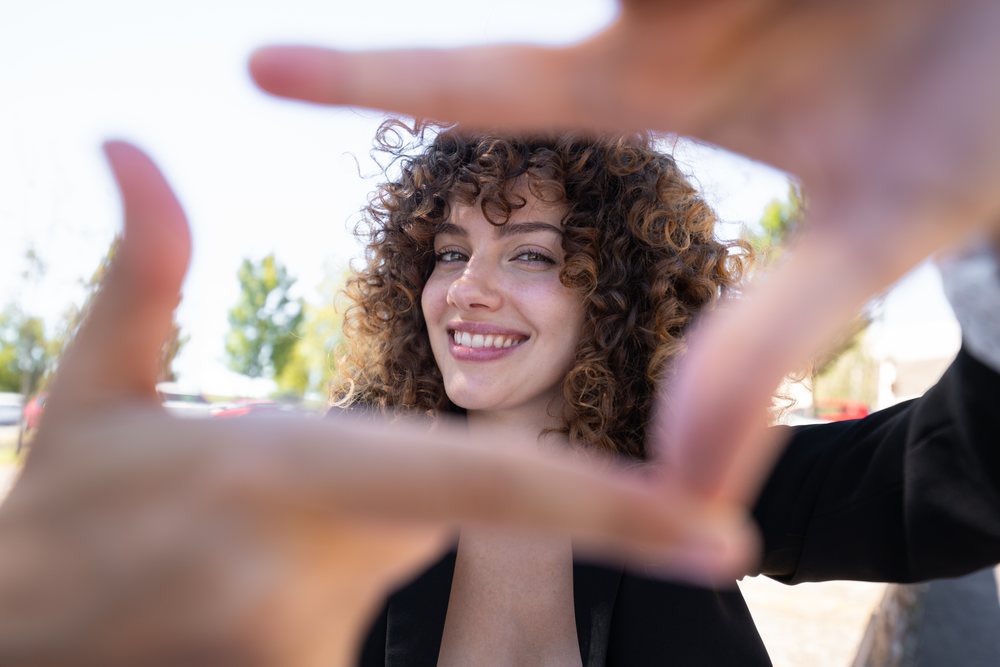 Young woman with curly hair smiling and framing her face with her hands outdoors, businesswoman, traveling executive, Spain.
