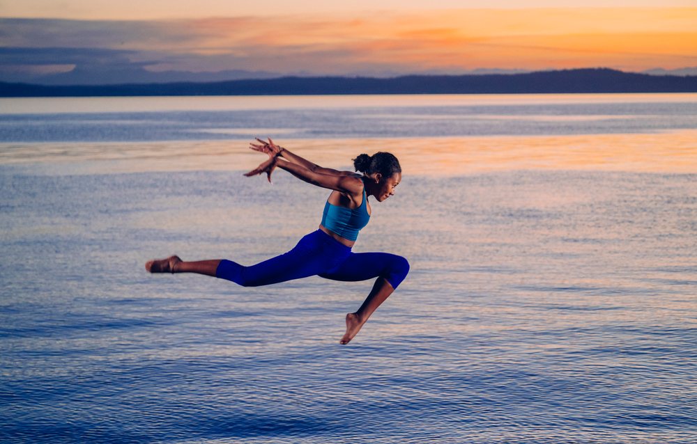 Woman performing a split jump over a lake at sunset, yoga, acrobatics, USA.