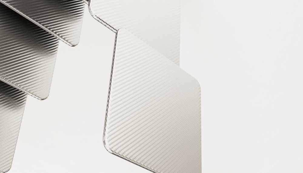 Stacked carbon fiber sheets with textured surfaces on a light background under studio lighting.