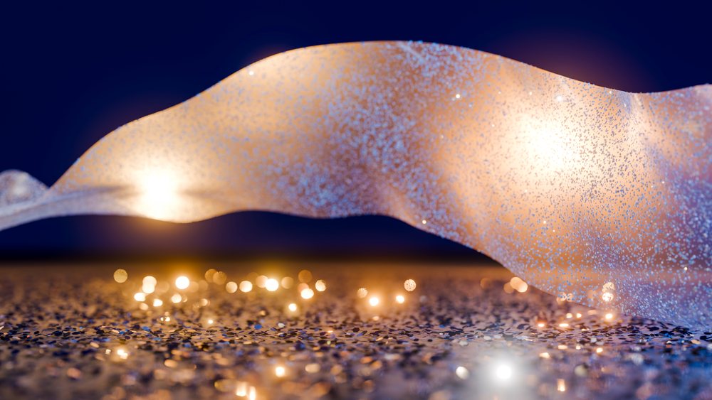 Glittery fabric with flowing folds is decorated by sparkling glitter particles and glowing light reflections against a dark blue background with warm orange and white glows.