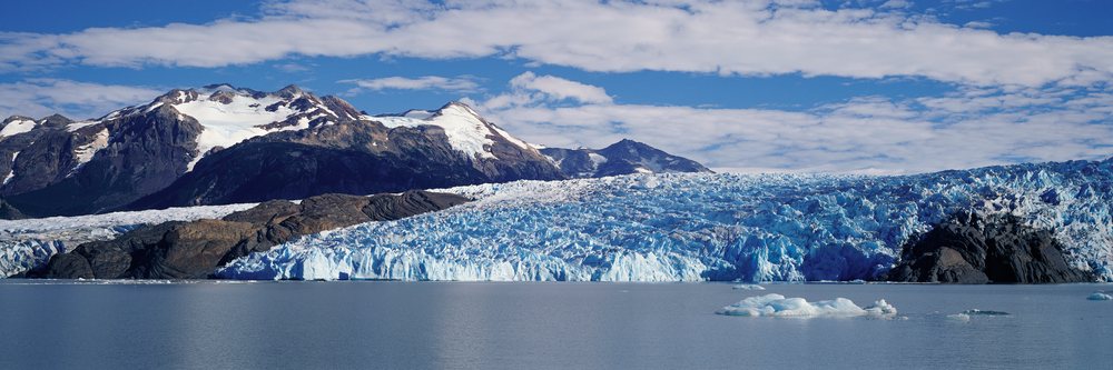 Glacier flowing into Lago Grey surrounded by snow-capped mountains and floating icebergs, Torres del Paine National Park, Chile.