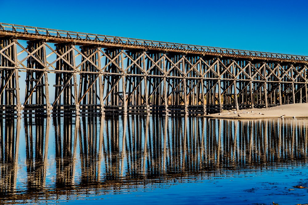 Wooden pier extends over calm water with seagulls resting on sandy shore under clear blue sky and, northern, Oregon, California, USA.