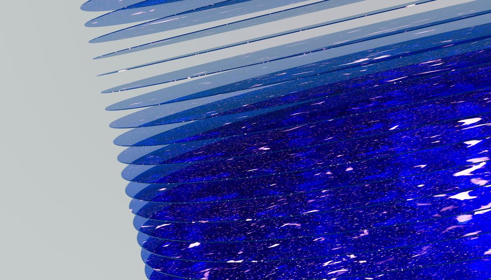 Blue glass sculpture composed of stacked, curved layered panels with reflective texture against a minimal grey background in a studio environment.
