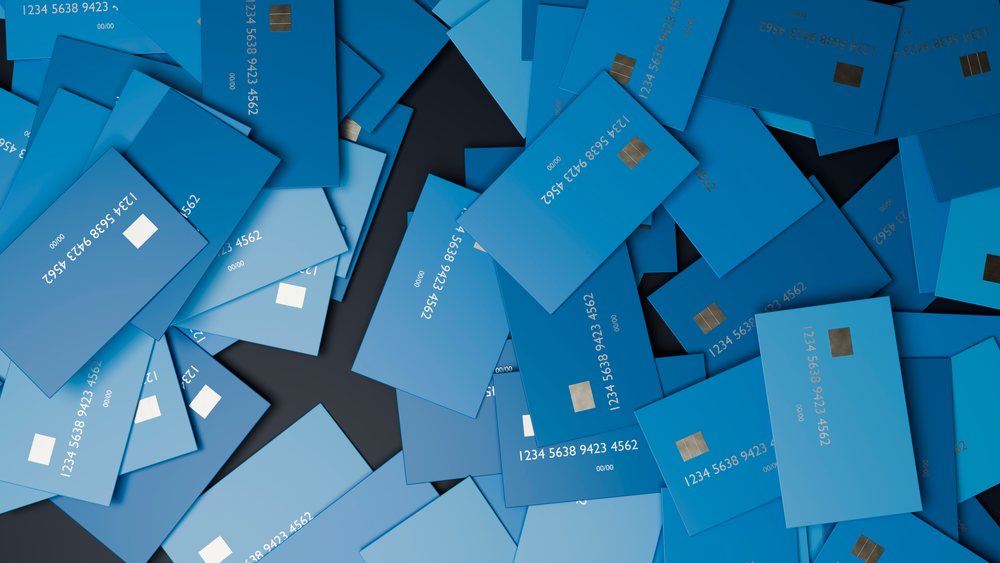 Multiple blue credit cards with visible card numbers and embedded chips stacked irregularly on a dark surface.
