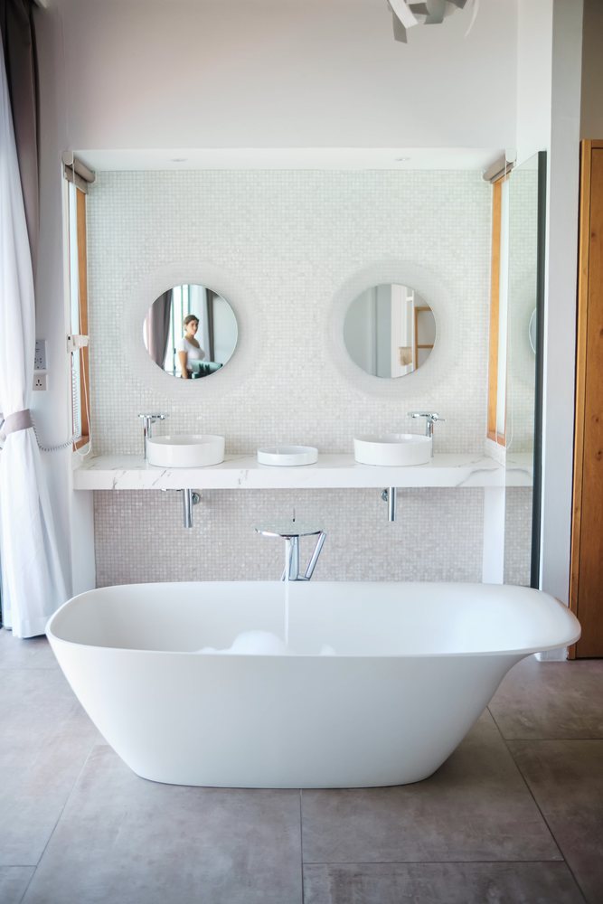 Modern bathroom interior featuring a white freestanding bathtub and double sinks with round mirrors located in the, Maldives.