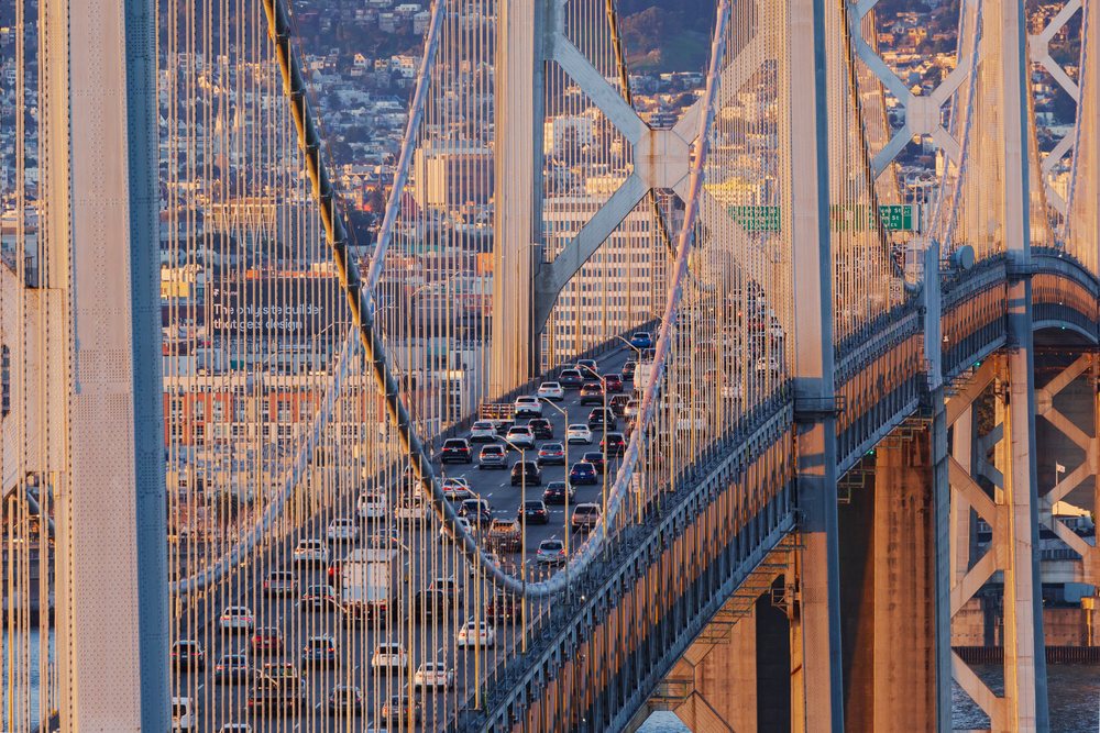 Rush hour traffic on the San Francisco Bay Bridge at Sunrise showing multiple vehicles on a suspension bridge over water with urban buildings in the background, City, Cityscapes, City Life, California, USA.