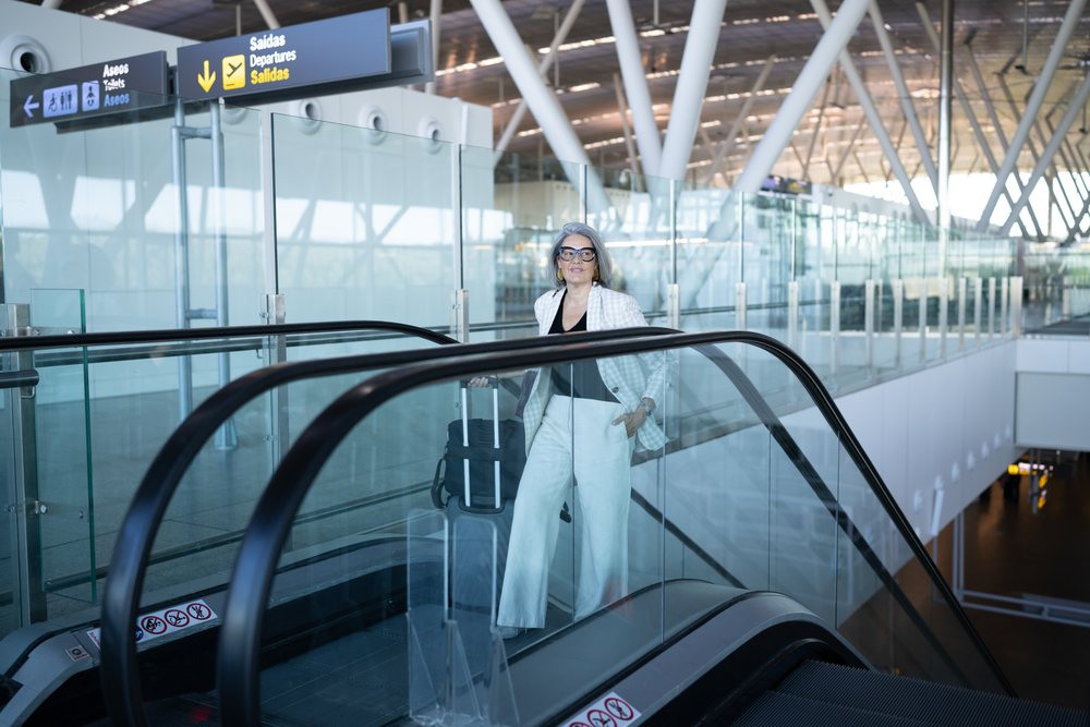 Businesswoman rides an escalator with luggage toward departures inside a modern Madrid airport terminal, Spain.