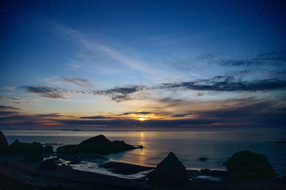 Star-filled night sky above a rocky coastline at twilight reflecting on calm ocean water at Oregon's Meyers Creek, USA.