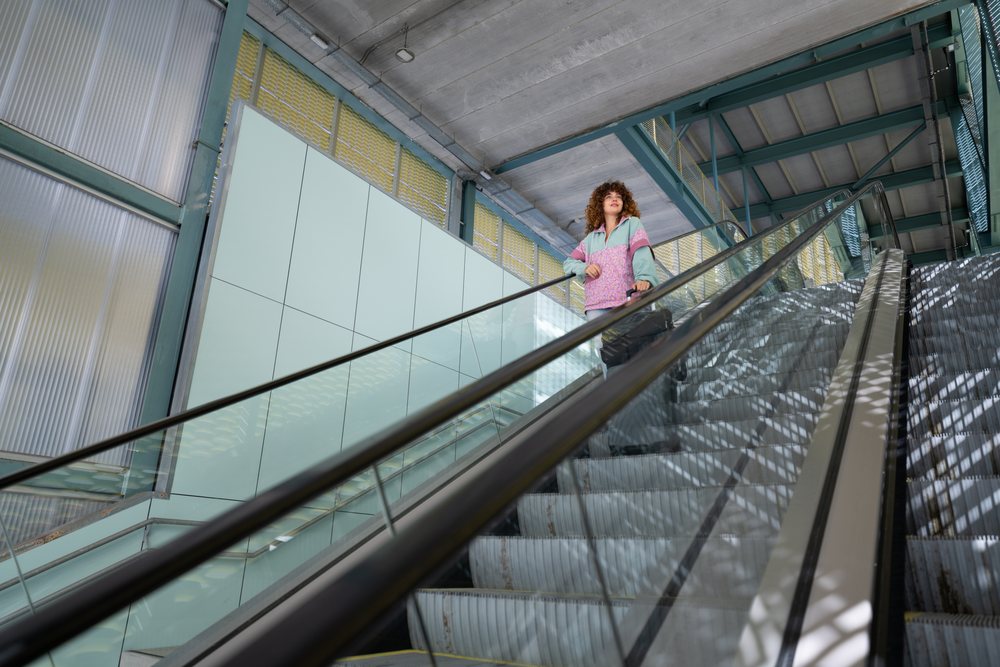Woman with curly hair pulls a suitcase on an escalator inside a modern building, Spain.