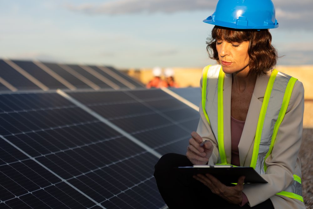 Solar energy expert wearing a blue helmet and high visibility vest inspects solar panels outdoors, Madrid, Spain.