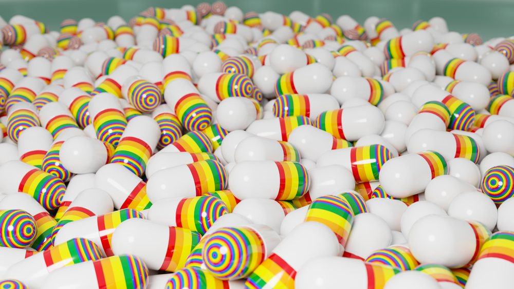 Close-up view of a large pile of white medication capsules with rainbow-colored stripes on a plain background.