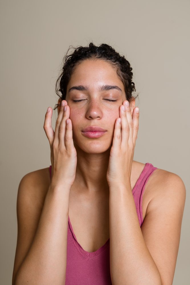 Woman with curly hair and freckles touching her face in a calm skin care moment against a neutral beige background, beauty shoot, Spain.