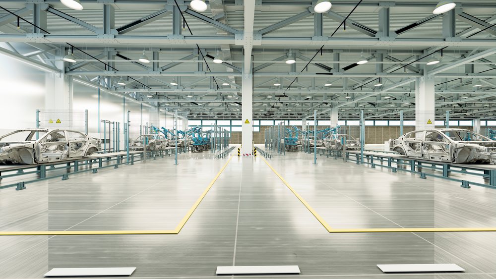 Car frames on conveyor assembly lines with multiple robotic arms in a large industrial automobile manufacturing factory interior.