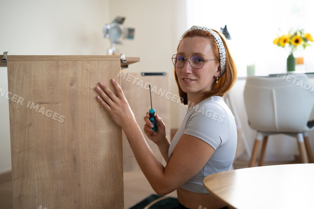 A white woman is assembling wooden furniture