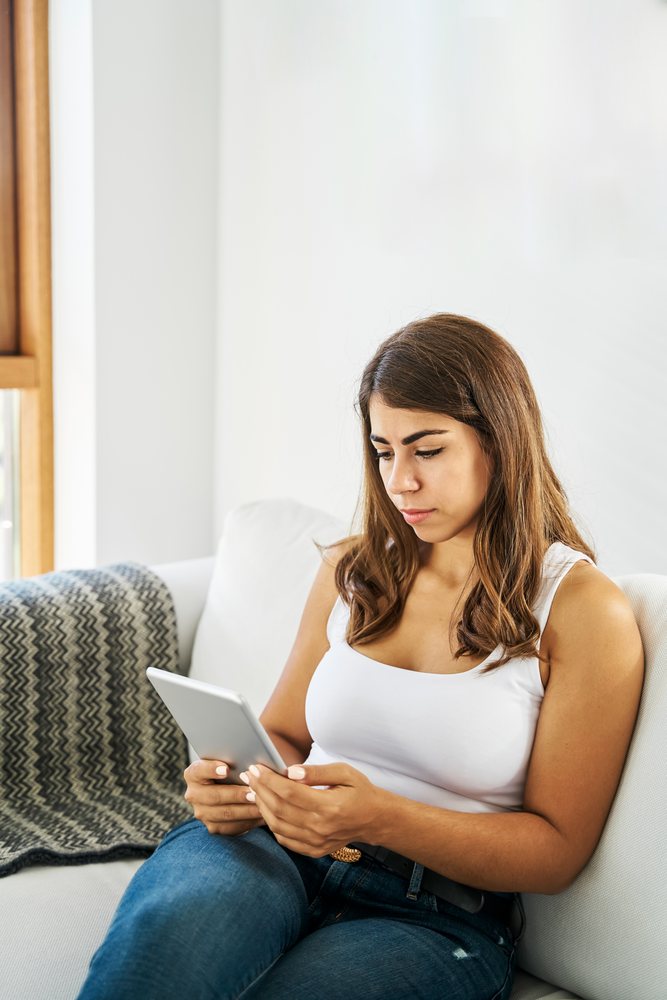A white woman uses a tablet while relaxing on a couch indoors
