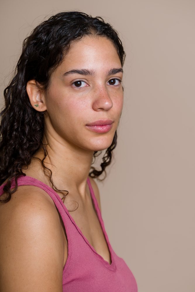 Portrait of a woman with curly hair and freckles wearing a pink tank top in a studio with a neutral background, beauty shoot, Spain.
