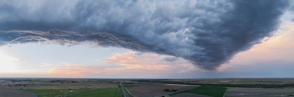 Storm cloud formation stretches over farmland and road, during sunset in the United States Great Plains, Storm Chasing, Weather, Environmental, Sterling, Colorado.