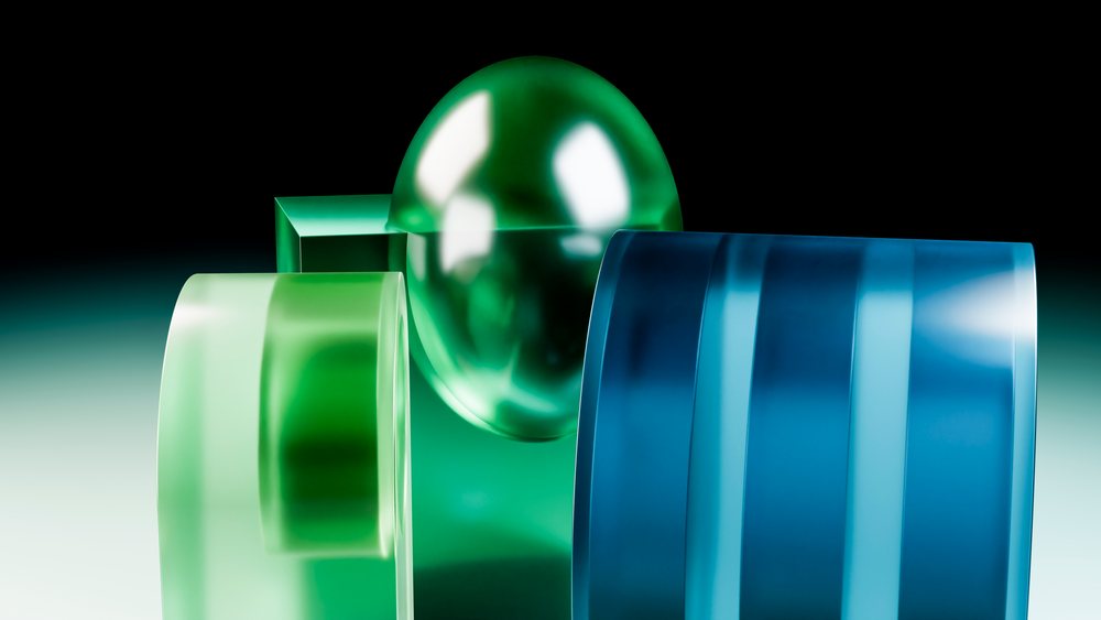 Abstract 3D illustration featuring green spherical, blue cylindrical, and green rectangular prism shapes with reflective surfaces and smooth textures.