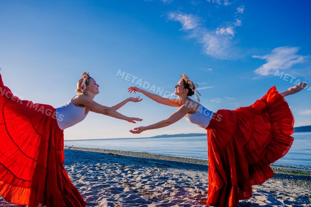 Two white women practice partner acrobatics yoga on a beach in WA, USA