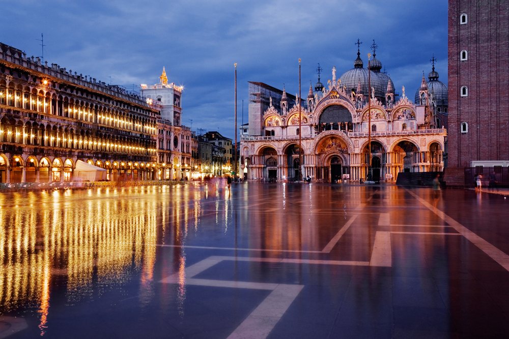 St Mark's Square, illuminated at evening with reflections on wet pavement and historic architecture, Venice, Italy.