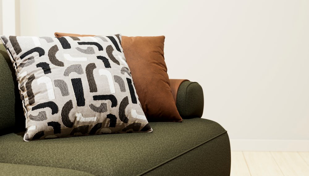 Two decorative pillows, one patterned and one brown, sit on a green modern sofa in a minimalist living room.