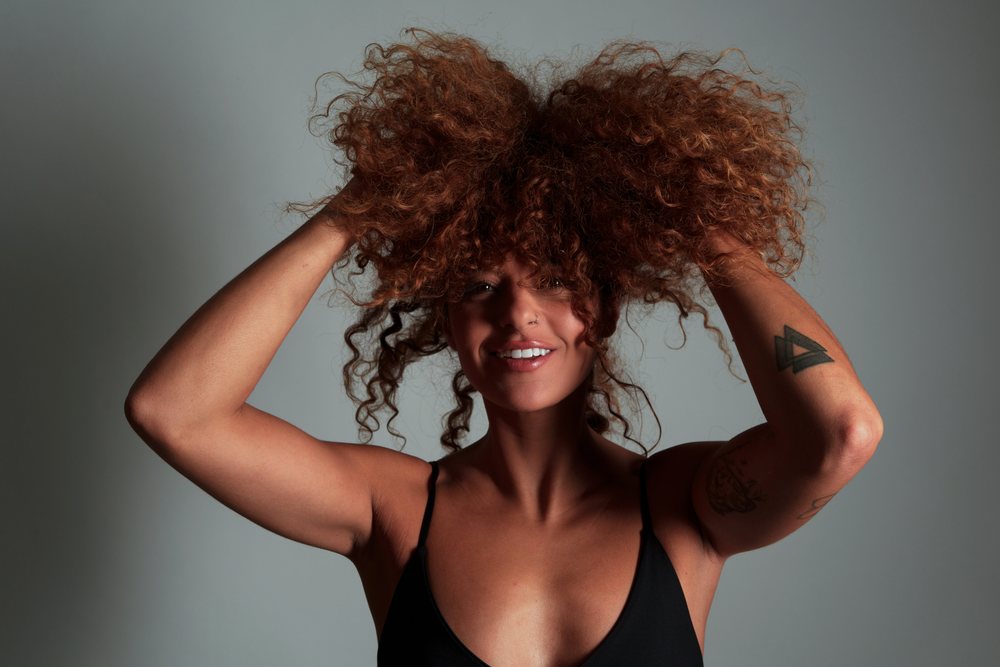 Woman with curly reddish hair and tattoos smiles in a studio, Malaga, Spain.