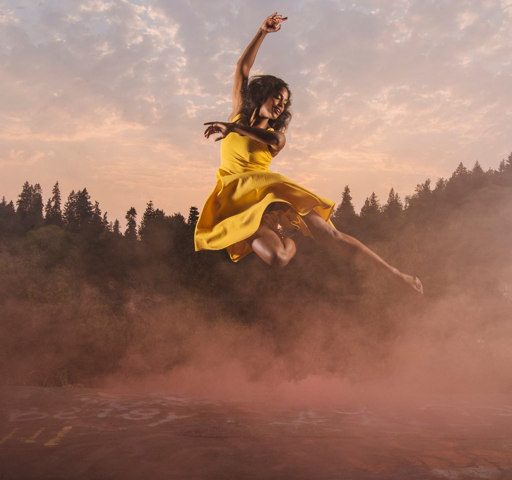Woman wearing a yellow dress jumps outdoors at sunset, USA.