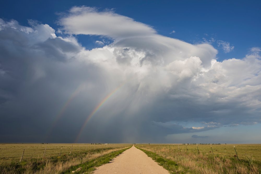 Supercell storm with Double Rainbow visible over grassland and dirt road, Amistad, New Mexico, USA.