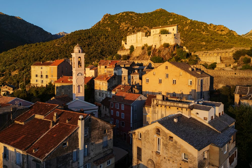 Sunrise over Corté, showing a castle on the hill and a church tower among historic buildings, Travel Photography, Corsica, France.