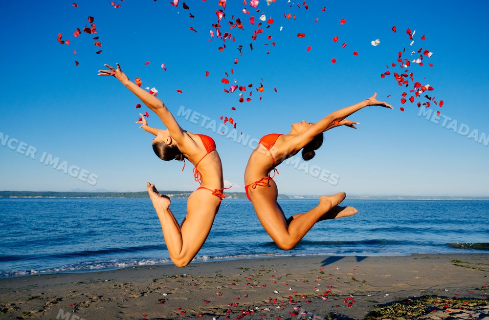 Two women jump on a sunny beach throwing rose petals in wa USA