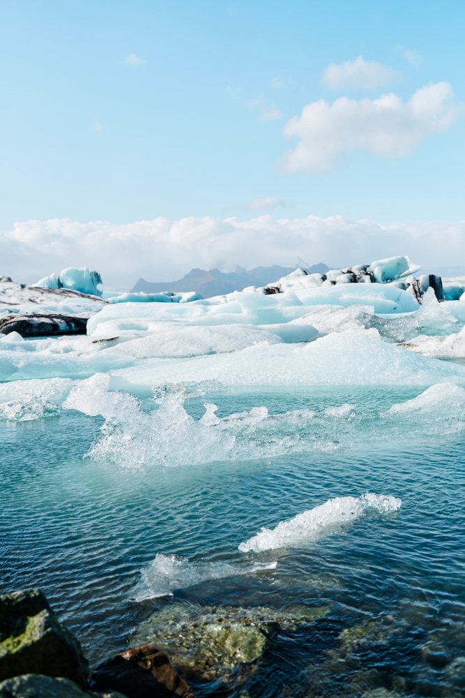 A natural scene of melting blue icebergs floating in clear arctic water under a blue sky, Iceland.
