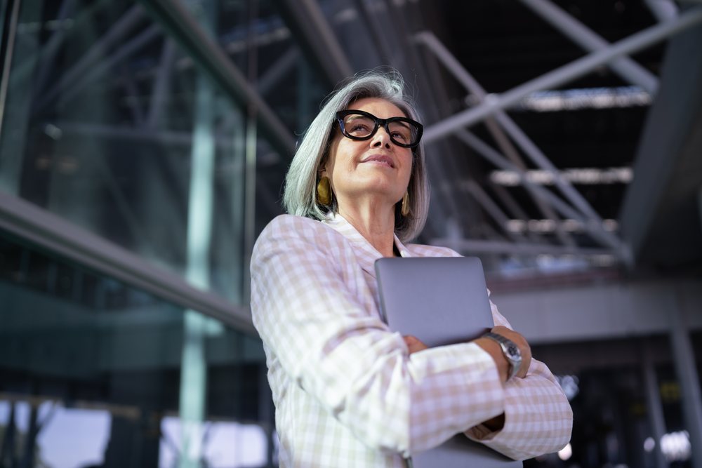 Businesswoman with gray hair and glasses holding a tablet inside a modern building, Spain, Madrid.
