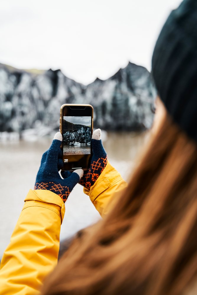 A white person takes a photo of rocky shoreline scenery