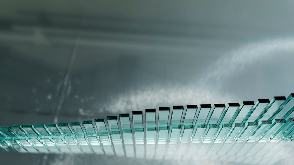 Close-up of stacked blue-green tinted glass panes with reflections in an industrial architectural setting.