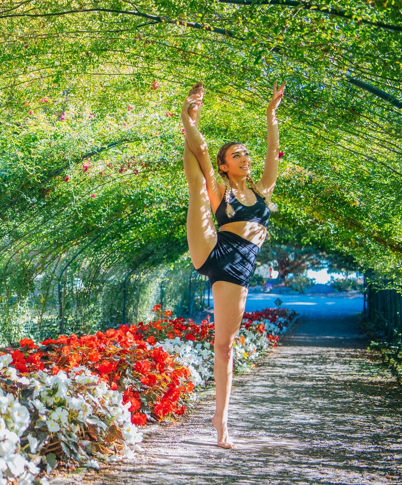 Woman contortionist performing stretching pose barefoot in a sunlit flower tunnel garden, Tacoma, WA, USA.