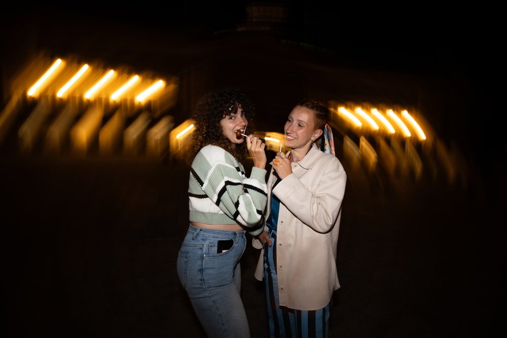 Two women outdoors at night, enjoying lollipops with light trails behind them, friendship, Santiago De Compostela, Spain.