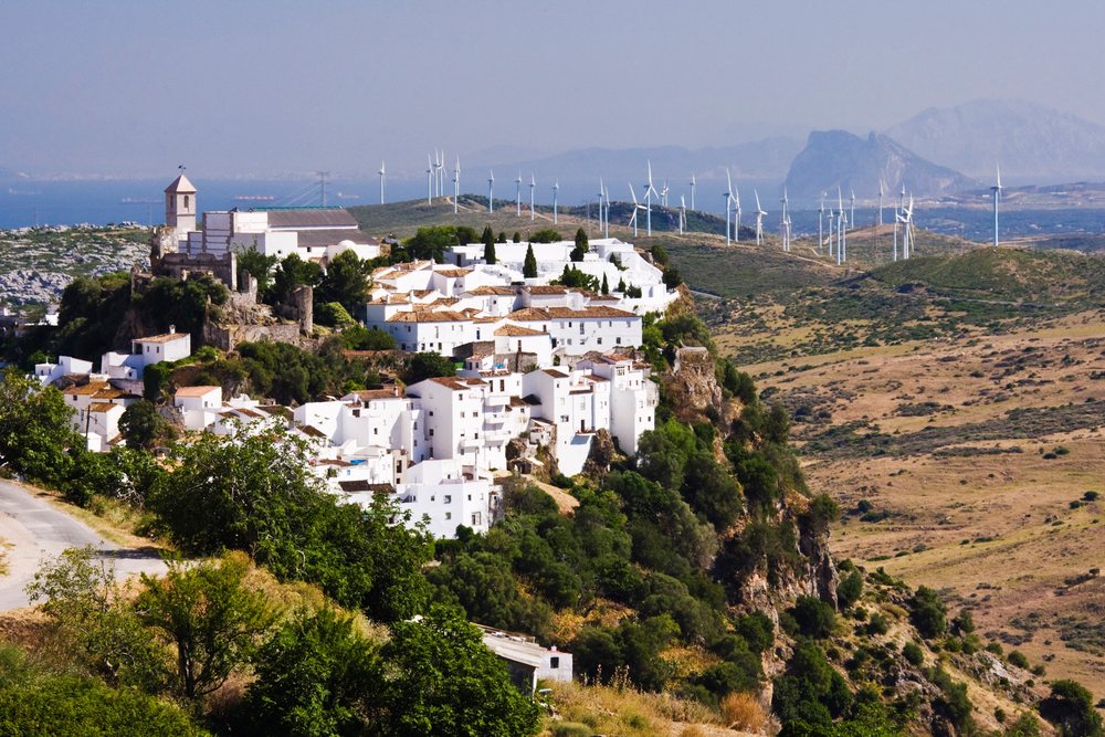 White buildings clustered on a hilltop with a church tower near wind turbines in a rural Andalusian landscape under clear skies, Andalucia, Spain.