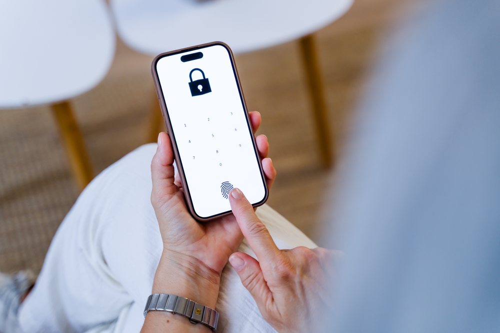 Person holding smartphone unlocking it with fingerprint on a digital lock screen indoors, Spain.