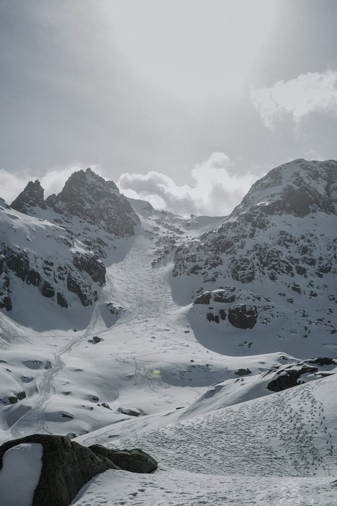 Snow-covered rocky mountain peak with ski tracks and footprints under a cloudy sky, mountaineering, climbing, landscape, Spain.