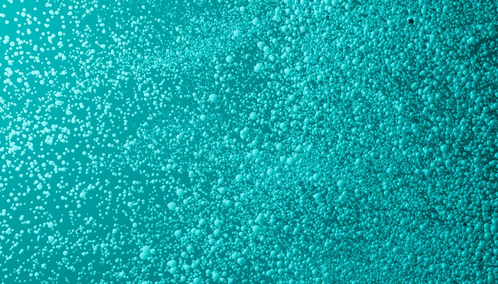 Close-up of turquoise liquid surface covered with numerous small bubbles forming a textured foam effect.