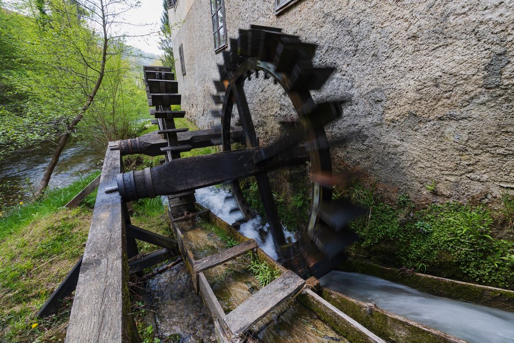Operating wooden Water Wheel attached to historic Kukovičičev Mlin mill, turning in flowing water outdoors, landscape, cityscape, Podsreda, Slovenia.