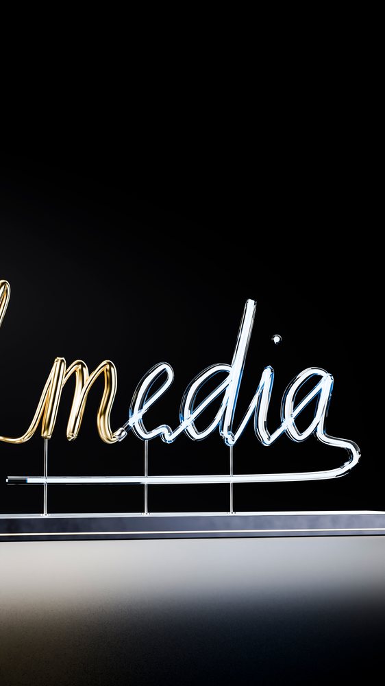 Neon sign glowing with white and gold light spells the word media against a black background.