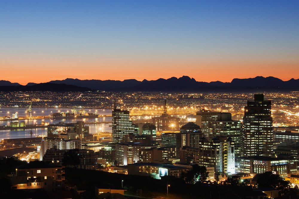 Cityscape of Cape Town showing illuminated buildings and silhouetted mountains, Western Cape, South Africa.