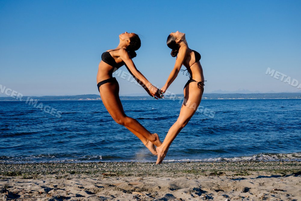 Two women doing acrobatic yoga poses holding hands on a beach