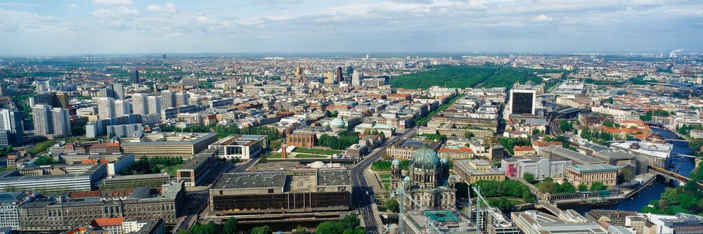 Aerial view of Berlin cityscape showing buildings, river, and green park under a partly cloudy sky, Overview Berlin, Germany.