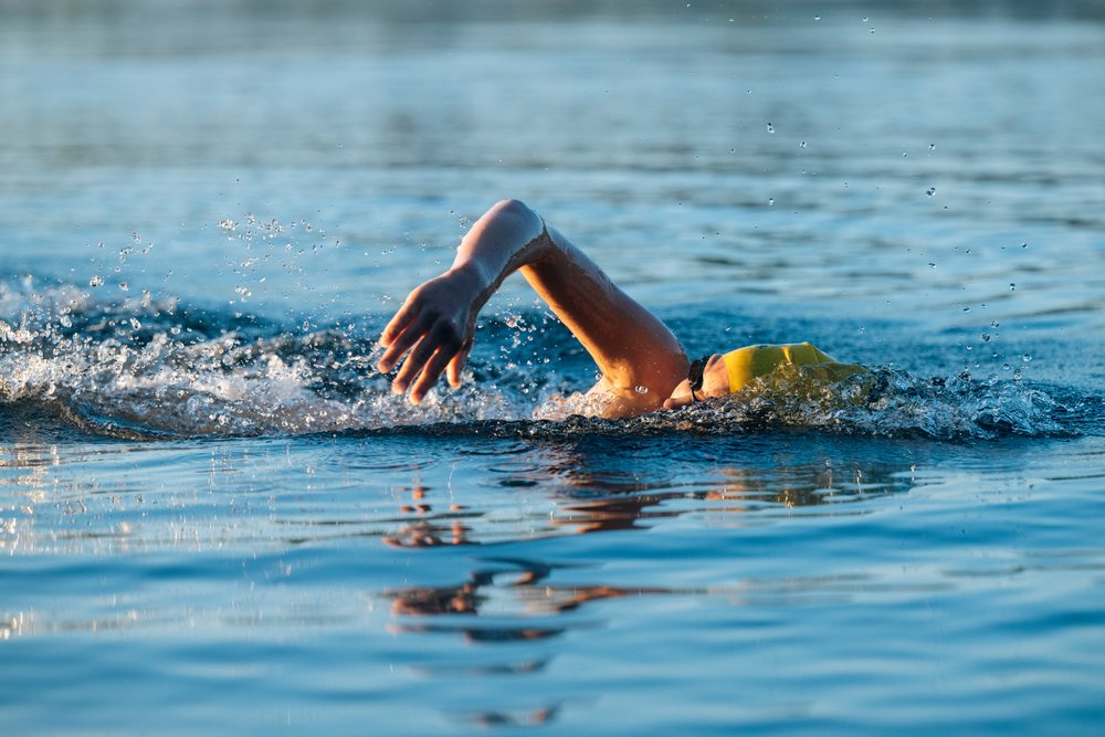 Swimmer wearing a yellow swim cap and goggles swimming freestyle in open water, USA.