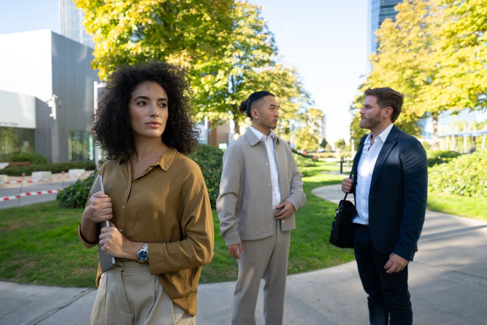Business professionals converse outdoors in an urban park on a sunny day near a sidewalk path with green trees, Madrid, Spain.