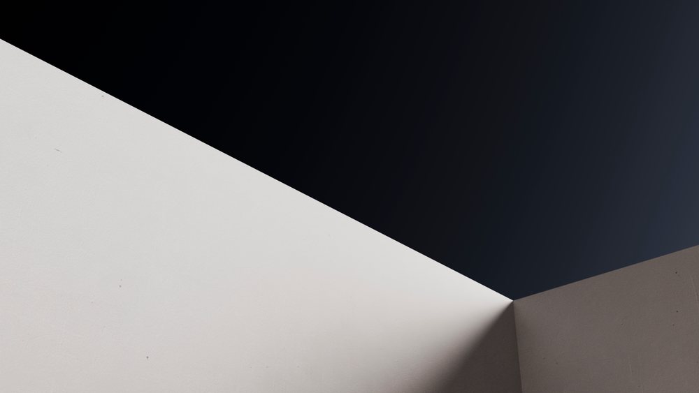 Corner where a white and gray wall meet under a dark background, showing clear contrast between light and shadow.